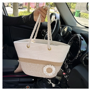 Close-up of beige woven tote bag with flower detail held by a model inside a car