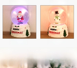 Close-up of glowing Christmas snow globe with Santa and Snowman resin base