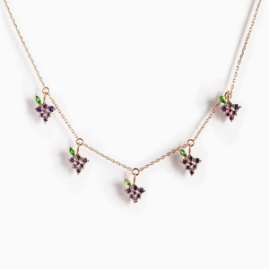 Close-up of golden necklace featuring five purple grape charms with green leaves