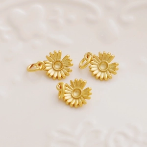 Three 18K gold-plated daisy flower charms for DIY jewelry making on soft pink background