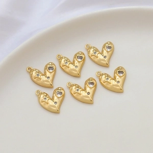 Six gold heart charms with zircon inlay set in a white ceramic dish for jewelry making