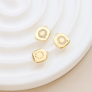 Detailed view of a gold-plated square pendant with sparkling zircon letter Q on a white stand