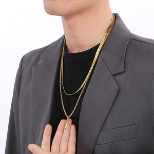 Detail of men's layered gold necklace with ankh cross pendant worn on grey suit
