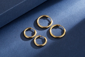 Detailed view of polished golden titanium hoop earrings in two sizes on blue background