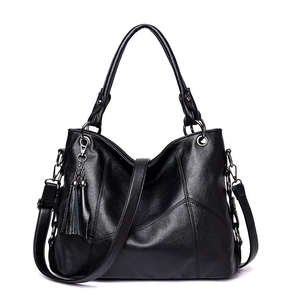 Detail of black soft leather handbag showing tassel charm and metallic buckle accents
