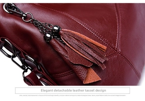 Detail of genuine cowhide leather texture and detachable tassel on a burgundy handbag
