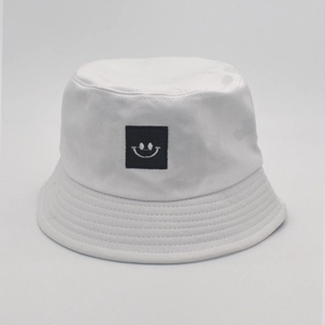 Detailed view of white cotton bucket hat with black embroidered smiley face patch