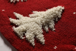 Close-up of red knitted fabric texture with white plush Christmas tree applique detail