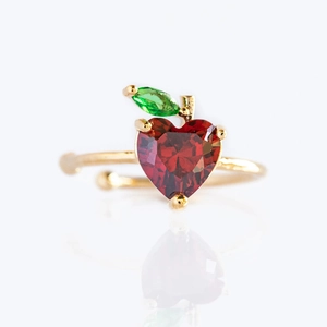 Macro shot of gold-plated apple ring with red heart gemstone and green leaf detail