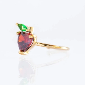 Macro shot of a gold apple ring featuring a red heart stone and green leaf detail