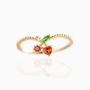 Macro shot of gold ring featuring red crystal cherry and green leaf stone setting