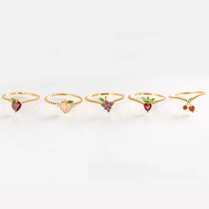 Detailed close-up of five gold rings with fruit gems on white reflective surface