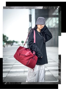 Red waterproof nylon duffle bag with shoulder strap shown carried by a model outdoors