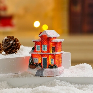 Close-up of LED glowing miniature Christmas house on snow surface with pine cones
