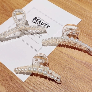 Detailed close-up of three clear acrylic hair claws with embedded pearls on a wood surface