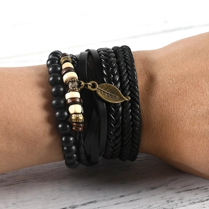 Close-up of stacked leather bracelets with matte beads and bronze leaf pendant