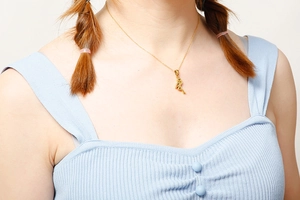 Close-up of golden necklace with a dancer pendant worn by a model on white background
