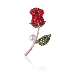 Macro shot of rose brooch detailing red and green crystal pavé with a central pearl
