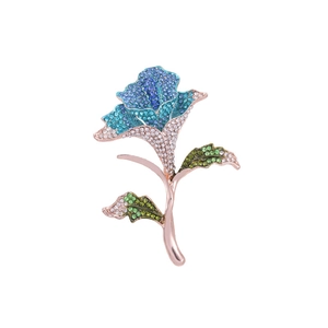 Close-up of rose brooch with gradient blue rhinestones and green leaves on rose gold stem