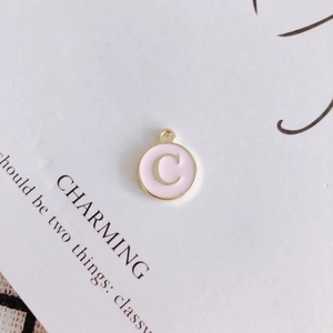 Macro detail of round pink enamel pendant with golden letter C and hanging loop