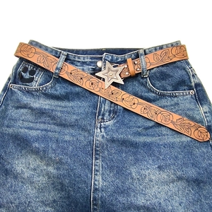 Vintage brown leather belt with rose embossing and a large silver star buckle on jeans