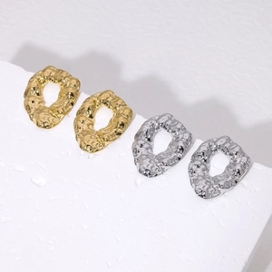 Minimalist hammered 18K gold and silver irregular stud earrings on white stone background