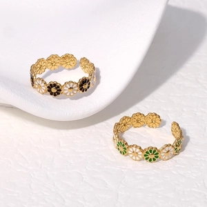 Detailed top view of two gold daisy enamel open rings on a white textured surface