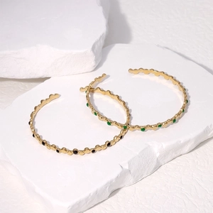 Detailed shot of open 18k gold-plated stainless steel bangles with black and green inserts