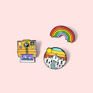 Set of three colorful enamel pins featuring a retro camera, rainbow, and mountain landscape