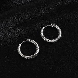 Macro shot of silver hoop earrings featuring a textured quilted pattern on black silk