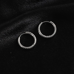Detailed close-up of twisted silver-colored titanium steel hoop earrings on black velvet