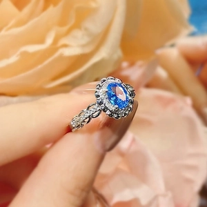 Elegant 3-carat oval blue sapphire ring with white accents on hand against floral background