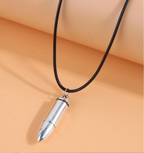 Close-up of a silver bullet pendant necklace with a black cord on orange background