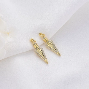 Golden arrow pendant charms with white zircon inlay on white textured fabric background