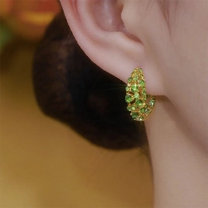 Elegant gold hoop earrings with green zircon stones worn by a model in a close-up side view
