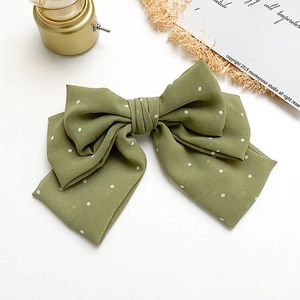 Green polka dot oversized bow hair clip on a clean white background with vintage props