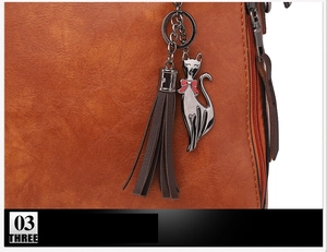 Détail du sac à main marron montrant le pendentif chat en métal et le gland en cuir