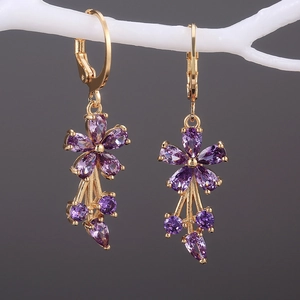Macro detail of gold flower earrings with purple cubic zirconia hanging on a white branch
