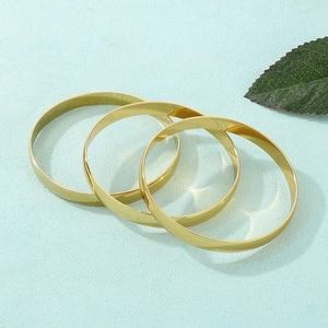 Three minimalist 8mm wide gold stainless steel bangles stacked on a light blue background