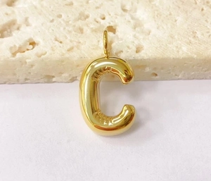 Macro shot of a chunky gold C-shaped letter charm on a natural stone surface