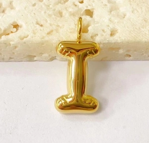 Macro shot of gold bubble initial letter I pendant on a textured stone surface