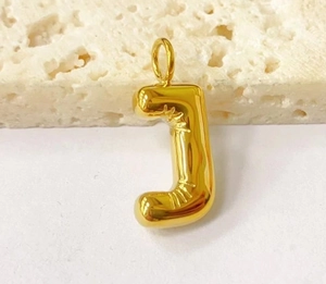 Macro shot of 3D puffy gold letter J pendant with high-shine metallic finish on stone