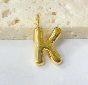Close-up of golden chunky bubble letter K pendant on a natural stone surface