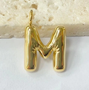Detailed macro view of a gold chubby bubble letter M pendant with hand relief design