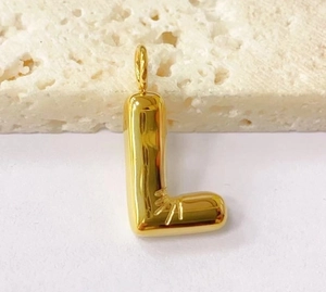 Detailed close-up of a golden puffy letter L pendant with sunburst engraving on stone