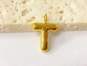 Detailed view of a golden bubble letter T pendant on a minimalist background