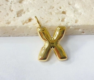 Detailed view of a polished gold letter X pendant charm on a textured stone base