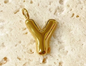 Close-up of a glossy gold bubble letter Y pendant on a textured white stone surface