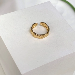 Macro detail of a gold minimalist open ring featuring an embossed diamond quilted texture