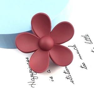Close-up of matte dark red flower hair claw clip with a resin finish on a blue background